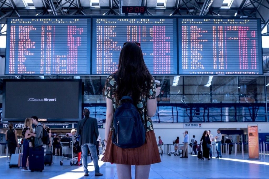 Young lady in a red dress looking up at the airport departures sceen