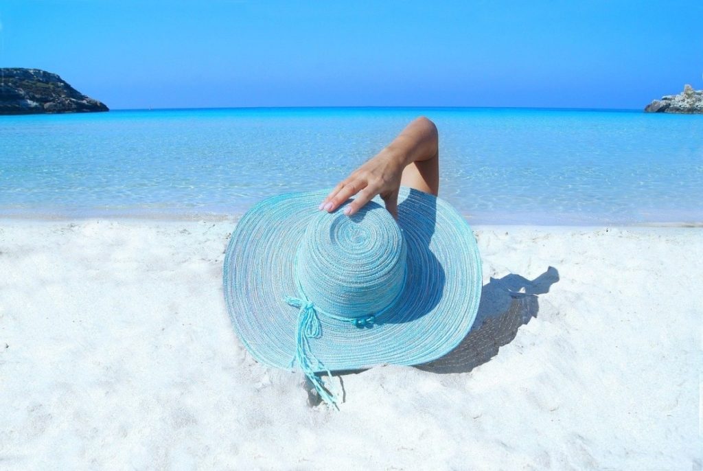 Woman on a white sand beach holding a blue sunhat - How to travel with a full time job