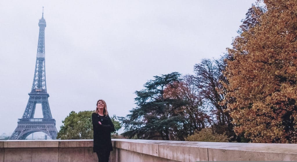 Eden wearing a black dress at the Trocadero in Paris with the Eiffel Tower in the background on a rainy day