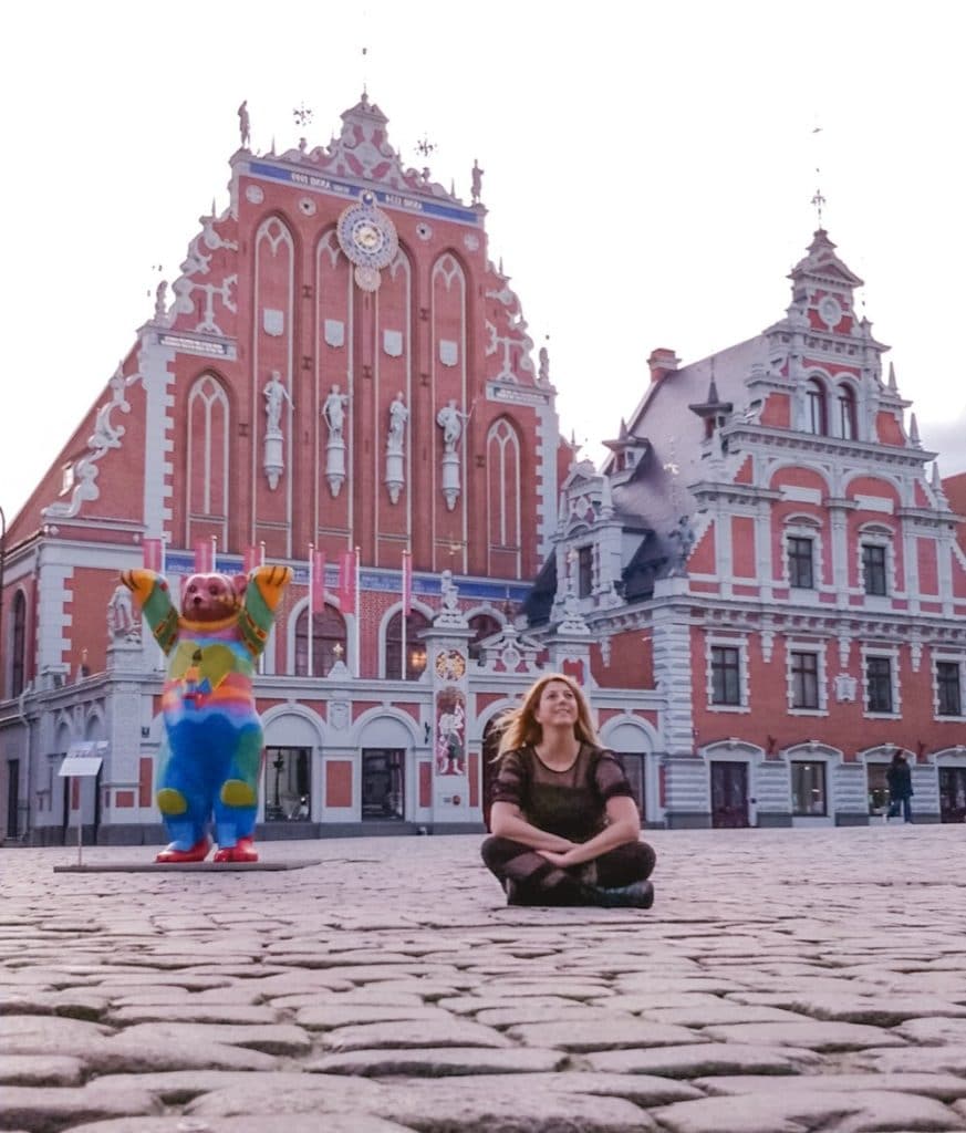 Eden Fite sitting on the ground in Riga, Latvia in front of the House of the Black Heads